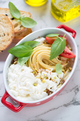 Spaghetti with stracciatella or stretched curd cheese and fresh green basil in a red serving pan,...