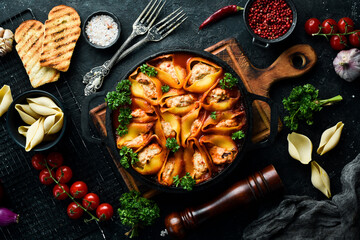 Pasta. pasta shells baked with meat, tomatoes and parmesan. In a frying pan. On a black stone background.