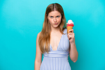 Young caucasian woman in swimsuit eating ice cream isolated on blue background with sad expression