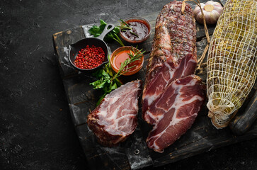 Dried and salted piece of meat. Prosciutto, jamon, on a black stone background. Top view. Free space for text.