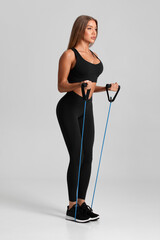 Fitness woman working out with resistance band on gray background. Athletic girl exercises with...