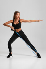 Fototapeta na wymiar Fitness woman working out with resistance band on gray background. Athletic girl exercises with expander