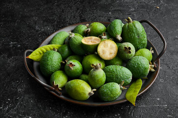 Feijoa. Fresh feijoa fruits on a tray. Top view, on a black stone background.