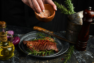 Steak with pepper and rosemary, in the hands of the chef. On a black stone background.