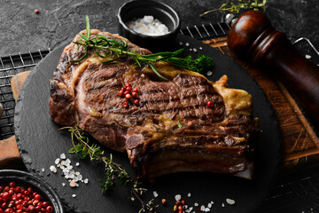 Juicy grilled steak on the bone cooked on the grill. Barbecue. On a black stone background.