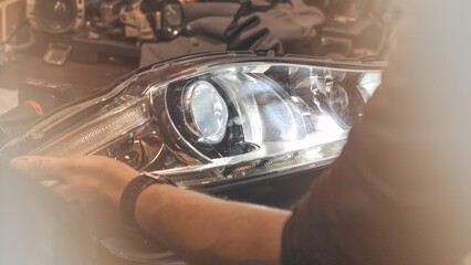 A car headlight in the hands of a man in close-up on a desktop background. An auto mechanic holds the headlight of the car. The concept of car repair in a car service. Dismantled headlight close-up. © Dmitry Presnyakov