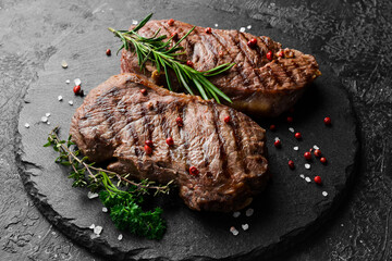 Two juicy rib eye steak, herbs and spices. On a black stone background.