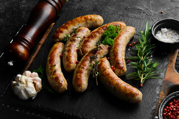 Grilled chicken sausages with rosemary and spices. Barbecue. On a black stone background.