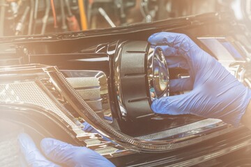 A mechanic wearing rubber gloves installs an LED lens into the headlight housing. Car headlight during repair and cleaning. The mechanic restores the car headlight.