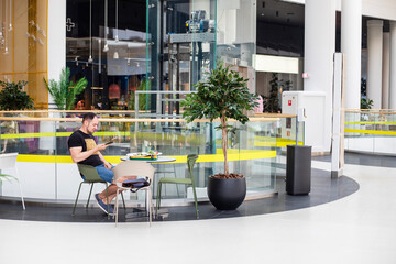 young man eats in a modern interior in the tcr and writes a message with green plants close-up....