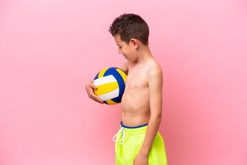Little caucasian boy playing volleyball isolated on pink background with happy expression