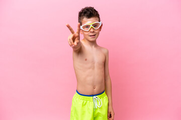 Little caucasian boy wearing a diving goggles isolated on pink background smiling and showing victory sign © luismolinero