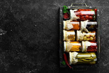 Jars of tasty pickled vegetables in a box. Food stocks in case of crisis. On a stone background. Top view.