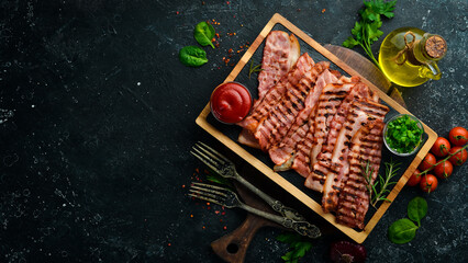 Fried pieces of bacon on a black stone board. Top view. Free space for text.
