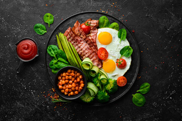 English breakfast: chickpeas, avocados, scrambled eggs, bacon vegetables on a black stone plate. Top view. Free space for text.