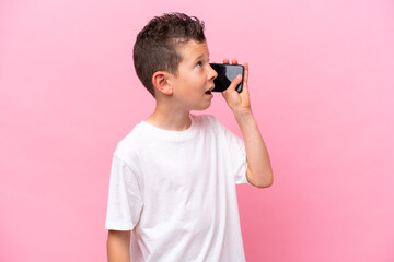 Little caucasian boy isolated on pink background keeping a conversation with the mobile phone
