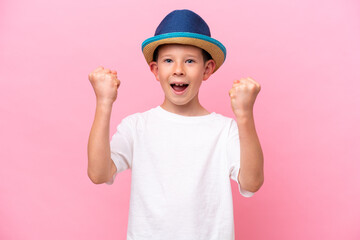 Little caucasian boy wearing a hat isolated on pink background celebrating a victory