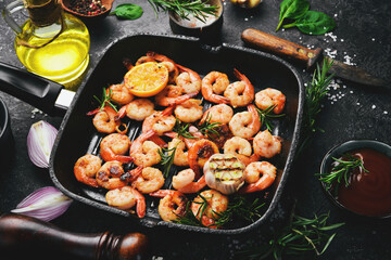 Fried shrimp with garlic and lemon in a pan. Seafood. On a black stone background.