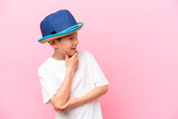 Little caucasian boy wearing a hat isolated on pink background looking side