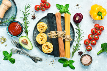Assortment of dry colorful spaghetti and pasta with cherry tomatoes and ingredients, on a gray stone background. Dry pasta. Top view. Free space for text.
