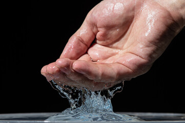 Fototapeta premium Water pours from the hand onto the surface of the water on a black background. Clean drinking water.