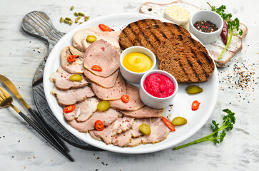 Sliced smoked meat and salami with sauce on a white plate. Top view.