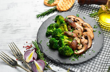 Organic food. Fried mushrooms and broccoli on a black stone plate. Rustic style. Top view.