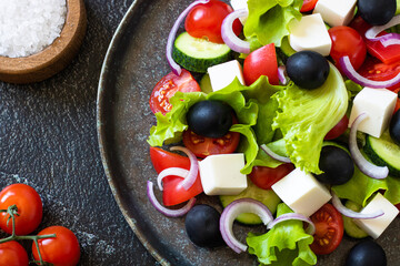 Greek salad on a round dish close-up, cherry tomatoes and salt nearby.