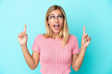 Blonde Uruguayan girl isolated on blue background surprised and pointing up