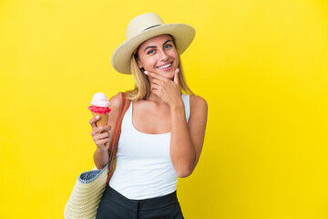 Blonde Uruguayan girl in summertime holding ice cream isolated on yellow background happy and smiling