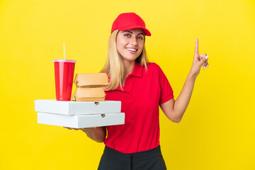 Delivery Uruguayan woman holding fast food isolated on yellow background showing and lifting a finger in sign of the best