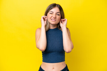 Young Rumanian woman isolated on yellow background frustrated and covering ears