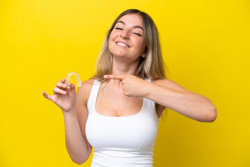 Young Rumanian woman holding envisaging isolated on yellow background and pointing it