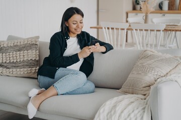 Fototapeta premium Happy woman relaxing with mobile phone and reading messages on comfortable couch in living room.