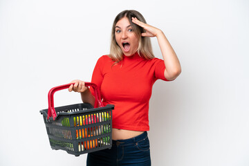 Young Rumanian woman holding a shopping basket full of food isolated on white background with surprise expression