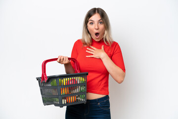 Young Rumanian woman holding a shopping basket full of food isolated on white background surprised and shocked while looking right