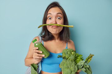 Boost your immune system. Surprised funny young Asian woman pouts lips with asparagus uses fresh green vegetables for making detox beverage keeps to healthy diet poses with homemade smoothie