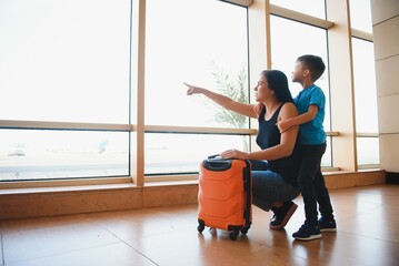 Family at airport before flight. Mother and son waiting to board at departure gate of modern international terminal. Traveling and flying with children. Mom with baby and toddler boarding airplane.