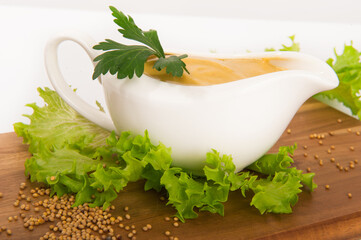 Mustard in a gravy boat with lettuce on a wooden board