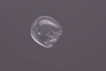 Drop of cosmetic transparent gel on a grey background. The texture of the serum, heir gel or hyaluronic booster.