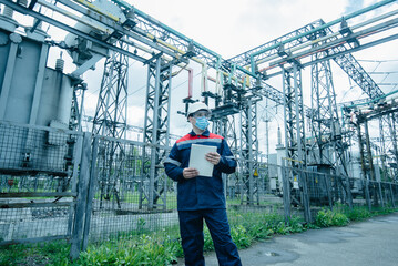 A masked power engineer during a pandemic inspects the modern equipment of an electrical substation before commissioning. Energy and industry. Scheduled repair of electrical equipment.