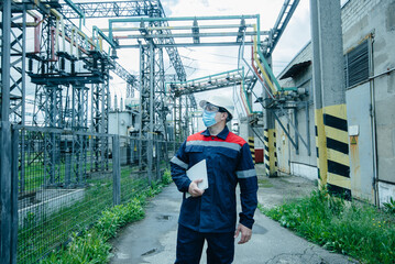A masked power engineer during a pandemic inspects the modern equipment of an electrical substation...
