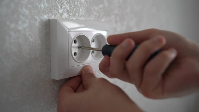 Electrician is using a screwdriver to remove the wires to the electrical plug on a wooden wall. Person checking the outlet voltag. Hand work of an electrician installing a power socket. 