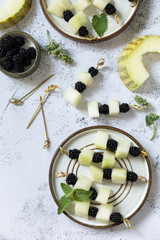 Festive summer snack of fruit and berry canapes. Vegan food. Canapes with melon and blackberries on a stone tabletop. View from above. Copy space.