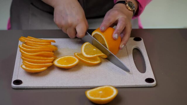 A young woman in the kitchen slicing oranges with a knife