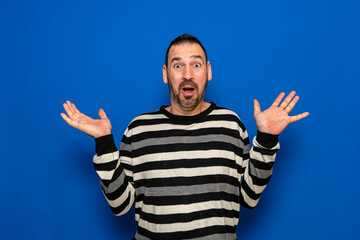 Naklejka premium Handsome bearded man in striped sweater standing over blue background scared and shocked with surprise expression, fear and excited face