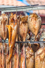 Hanging smoke-dried various fish in a fish market just smoked with hardwood wood chips in a smoker and ready to eat, vertical