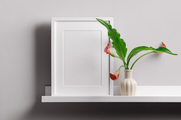 Vertical white frame mockup on shelf with calla flowers