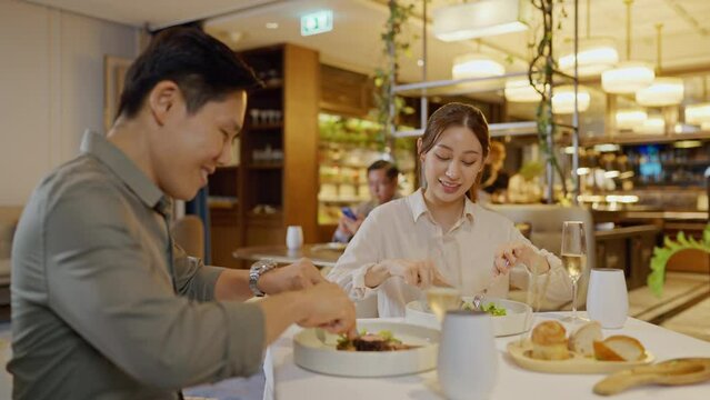 Asian couple having dinner at an upscale restaurant. Woman is taking pictures of food and showing it to her boyfriends.