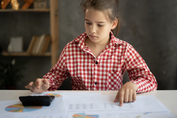 Little girl counting bills, calculating budget at home using calculator, working with financial documents at desk, paying bills online, managing